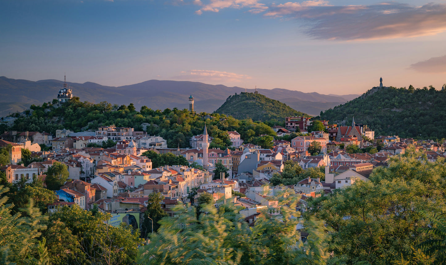 Panoramic view of Plovdiv, Bulgaria with colorful buildings, green hills, and distant mountains under a blue sky with scattered clouds